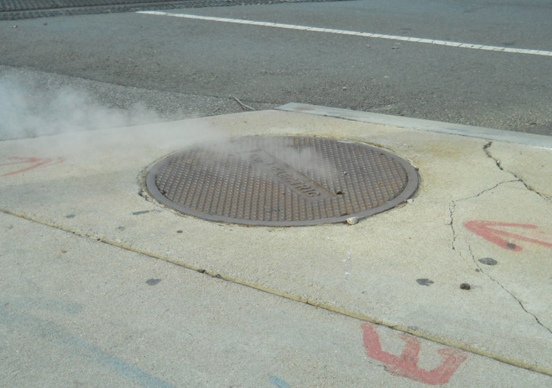 Hot manhole cover on sidewalk pavement poses a threat to pedestrians